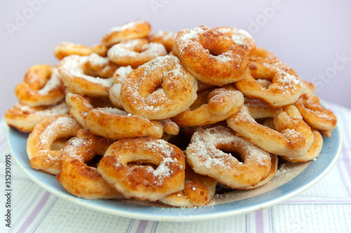 a pile of sweet Golden-brown doughnuts (doughnuts) with white powdered sugar lies in a white plate on a light background close-up