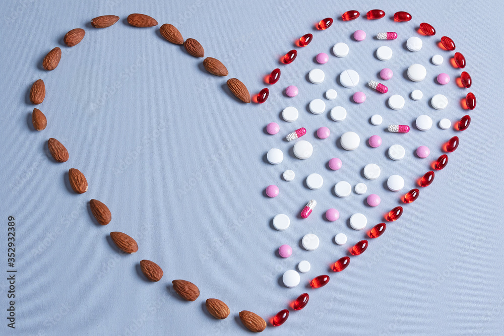 Healthy eating concept. Crooked heart made from pills and almonds. Healthy fats and red and white pills on gray background