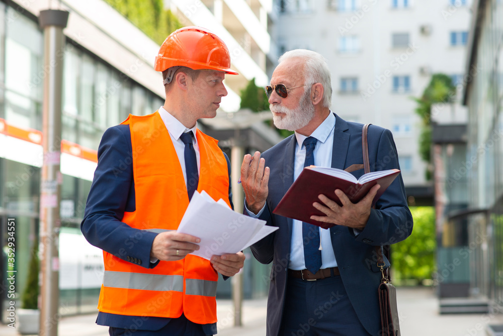 Senior man discussing something with engineer man with papers Senior man discussing something with engineer man with papers