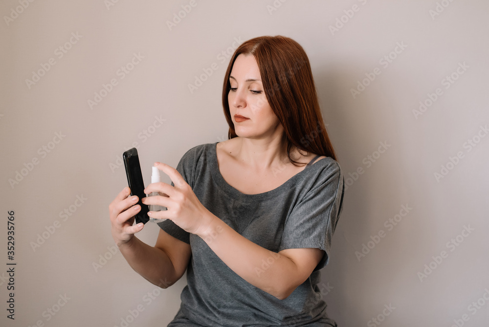 Woman is spraying alcohol disinfectant spray on smartphone, prevent infection of Covid-19 virus Woman is spraying alcohol disinfectant spray on smartphone, prevent infection of Covid-19 virus