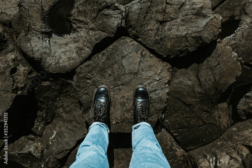 Looking down on female legs wearing black boots and blue jeans standing on pentagon shaped stone formations