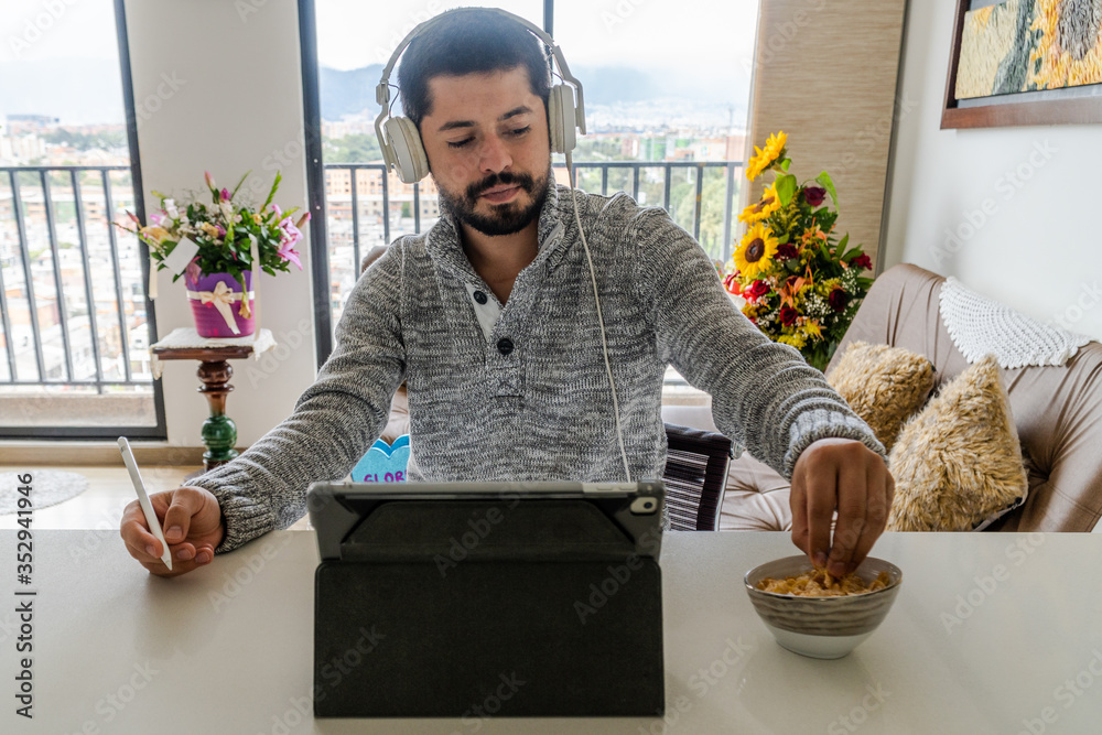Hombre con audífonos frente su tablet comiendo Hombre con audífonos frente su tablet comiendo