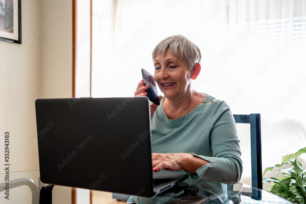 Caucasian senior woman working on computer and talking on the phone Caucasian senior woman working on computer and talking on the phone