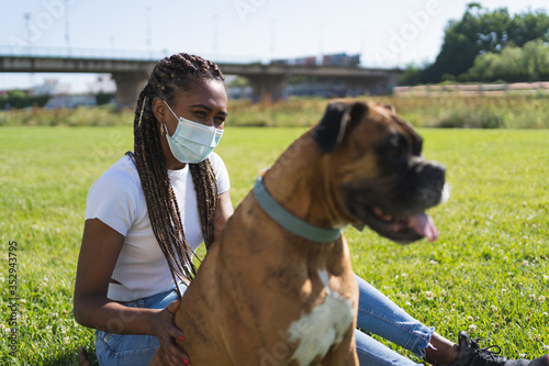 Selective focus on an ethnic african woman wearing a protective mask and sitting next to a boxer dog photo