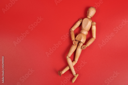 a full-length wooden man is lying on a red background in a relaxed position. A wooden puppet with crossed wooden legs in a reclining position