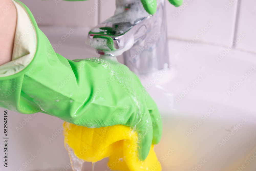 woman in gloves washes a sink and water tap in the bathroom woman in gloves washes a sink and water tap in the bathroom
