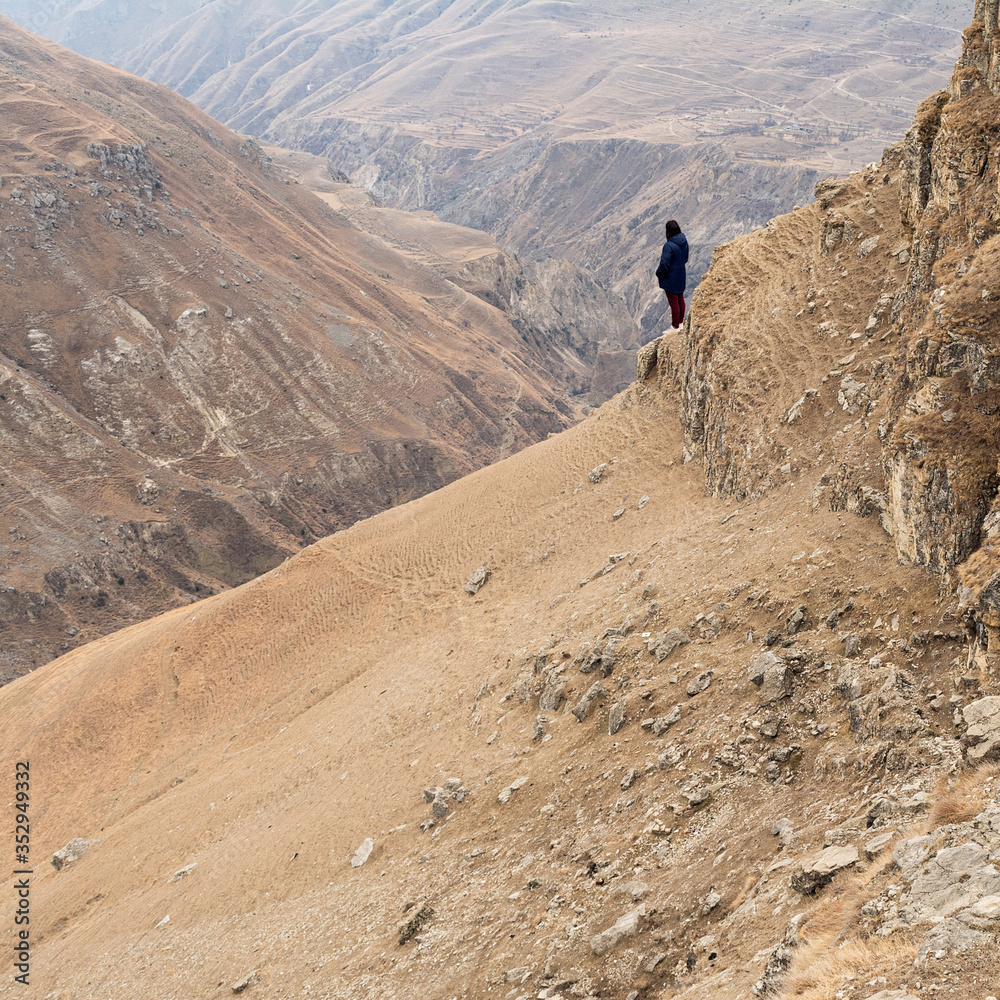 A girl in a blue jacket and burgundy jeans stands on the edge of the mountain amid a sandy canyon. Concept people, landscape, travel.