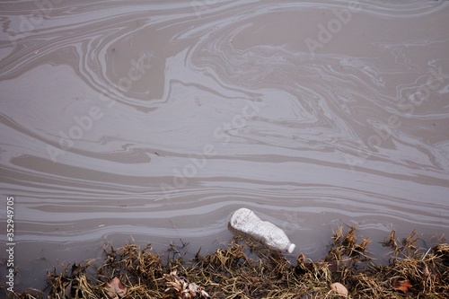 A discarded water bottle floats in a polluted stream.