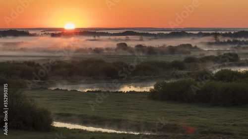 4k timelapse of the warm golden sun rising above the river and casting warm red color on the moving fog