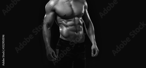 Muscular model sports young man on dark background. Black and white fashion portrait of strong brutal guy. Sexy torso. Male flexing his muscles. Sport workout bodybuilding concept. © KDdesignphoto