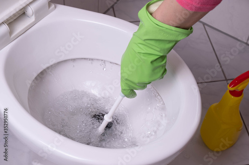 cleaning lady in the bathroom cleans a clogged toilet in green gloves