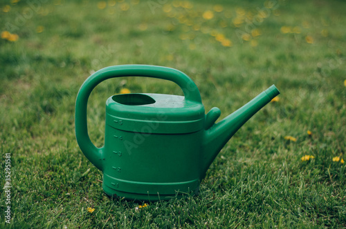 Multi-colored different sizes watering cans stand in a green garden. Little helper, gardener, spring crops, summer mood.
