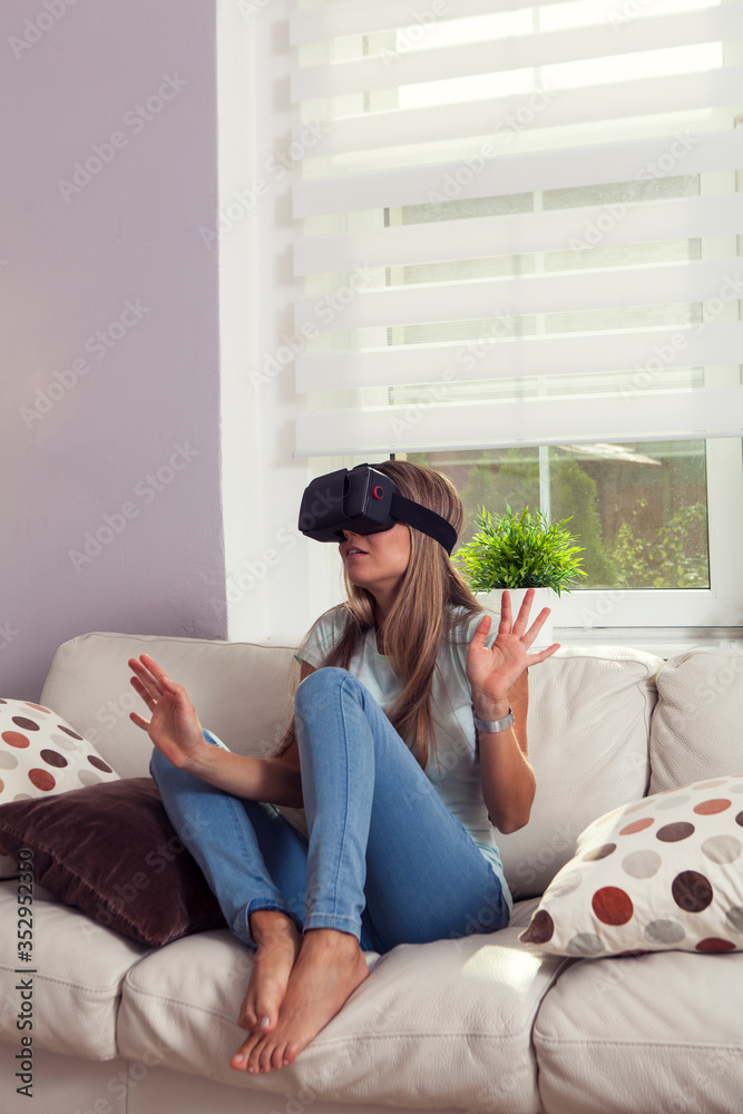 Young girl wearing jeans barefoot playing with virtual reality headset  seated on couch, she is a bit scared and confused foto de Stock | Adobe  Stock