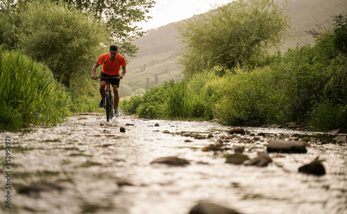 boy with orange shirt during a cycling adventure along a creek. Flare and light effect, scenic shot. Ideal for concept of fredoom, happiness and adventure. Splash of water photo