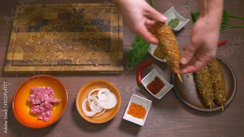 Lulia kebab, a dish of Georgian cuisine. Process of making kebab lula, top view. Chef cooks a lula kebab from raw minced meat and sprinkled with spices. Spices and ingredients stand on the table. photo