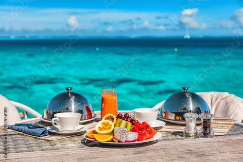 Fototapeta Naklejka Na Ścianę i Meble -  Vacation breakfast at luxury hotel room ocean view. Romantic honeymoon travel holiday in Maldives or Tahiti. Presentation of two plates, fruits, coffee, juice.