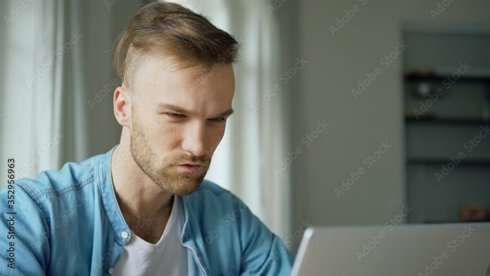 Medium shot of focused young man opening laptop computer, typing and thinking of problem solution at home Medium shot of focused young man opening laptop computer, typing and thinking of problem solution at home