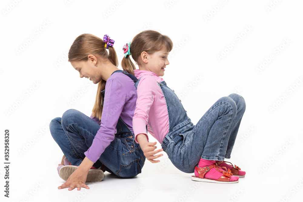 Children sitting on the floor have fun pushing their backs, isolated on white background Children sitting on the floor have fun pushing their backs, isolated on white background