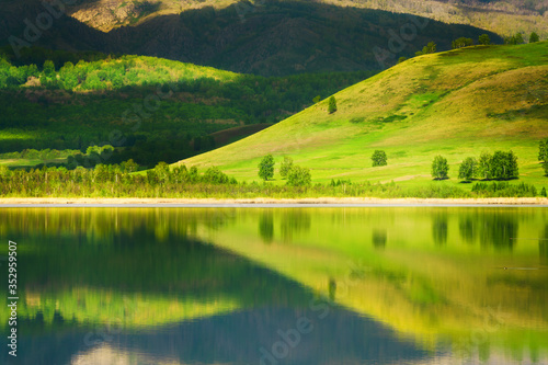 Green trees on the mountains and their reflections in the lake. Beautiful summer landscape. South Ural, Russia