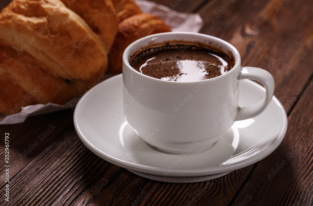 Cup of freshly coffee and tasty croissant on dark wooden table. Sweet and tasty breakfast. Cup of freshly coffee and tasty croissant on dark wooden table. Sweet and tasty breakfast.
