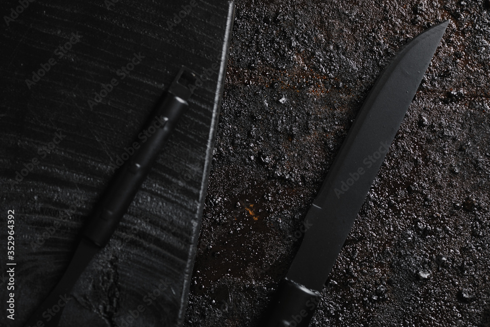 Knife and for on pice of black wood and black texturated background.