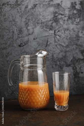 Pitcher with  glass and orange juice photographed with studio light on grey textured background.