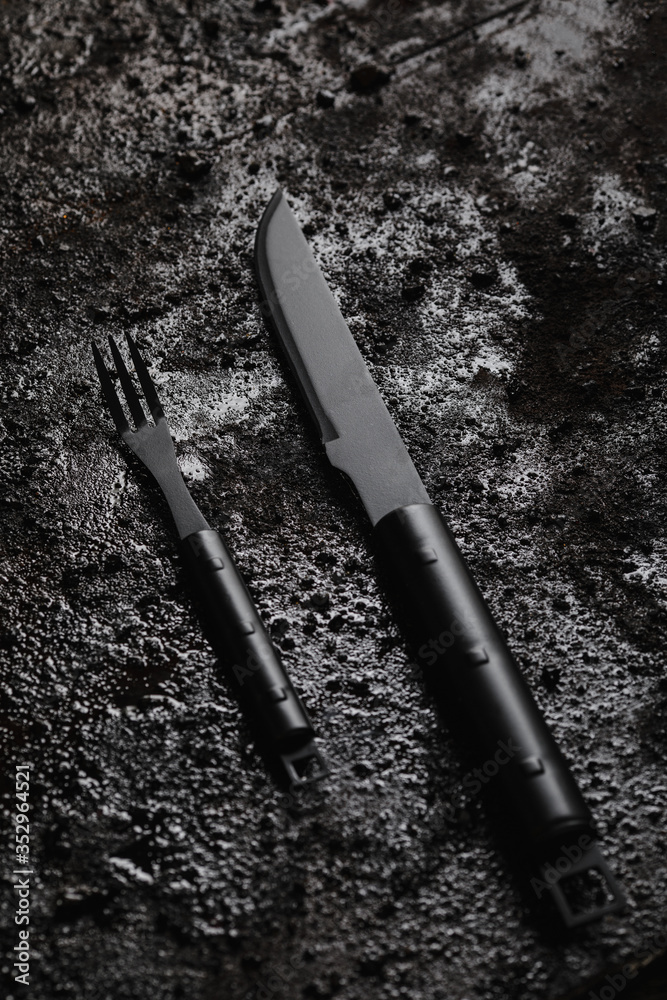 Knife and for on pice of black wood and black texturated background.