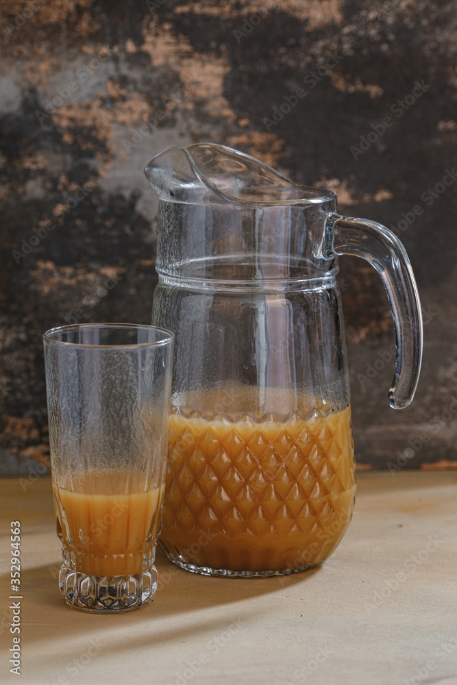 Pitcher with glass and orange juice on photographed with natural light on brown textured background.