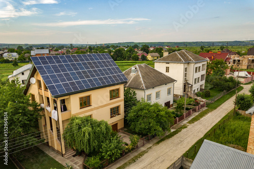 Aerial top view of new modern residential house cottage with blue shiny solar photo voltaic panels system on roof. Renewable ecological green energy production concept.