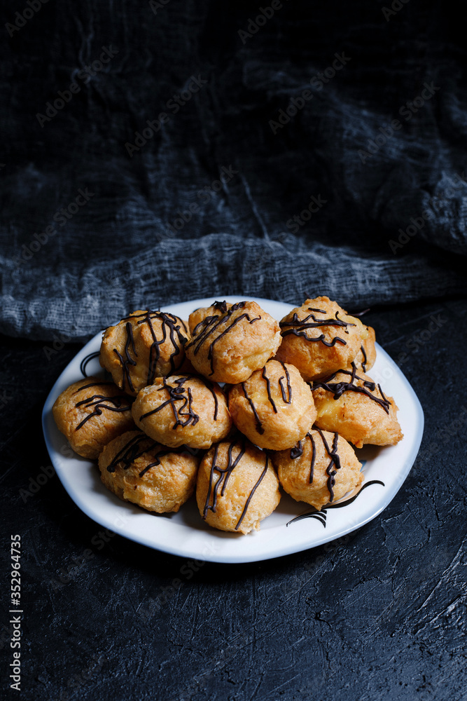 Delicious profiteroles on black textured background with a creative decoration.