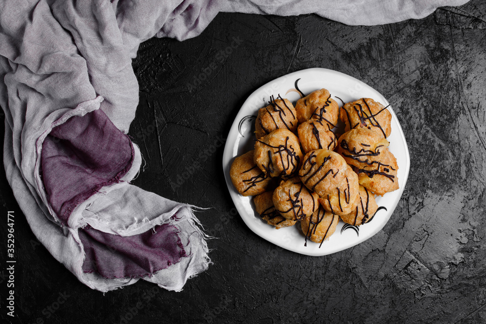 Delicious profiteroles on black textured background with a creative decoration.
