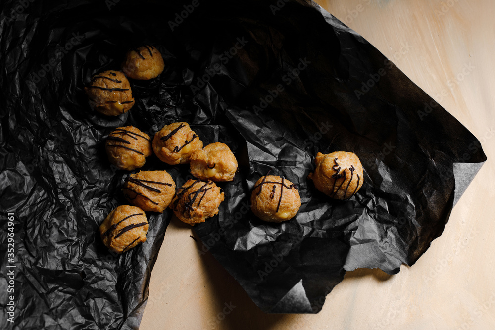 Delicious profiteroles on black textured papper and yellow background photographed with studio light.