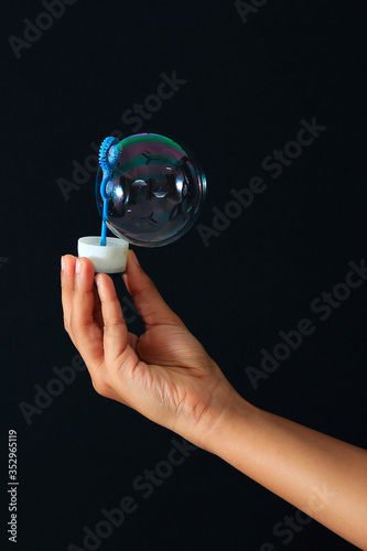 Rainbow soap bubble with hand holding bubble wand isolated on black