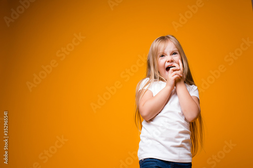 Little girl nibbles the fingers of her hands. The concept of bad habits in children on an orange background