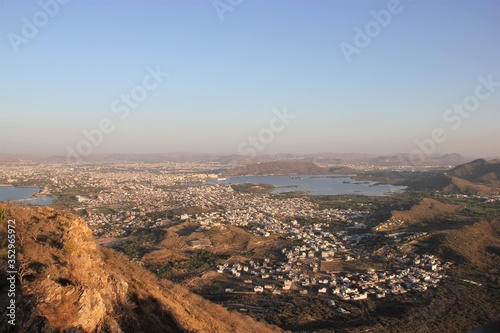 Panorama View of the City of Udaipur in Rajasthan, India, at Cloudless Sunset with a Dusty Yellow Background Hue and a Sprawl of Mostly White Houses in the Foreground
