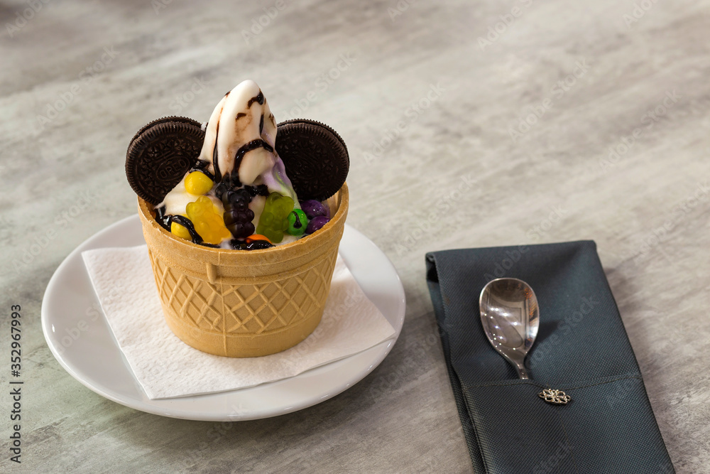 Ice cream dessert in wafer cup with chocolate cookies and creative decoration topping on blurred light copy space background. Ice cream dessert in wafer cup with chocolate cookies and creative decoration topping on blurred light copy space background.