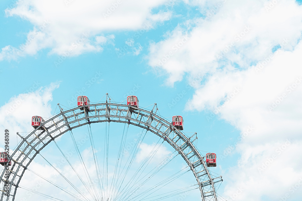 Gray ferris wheel with red booths against a blue sky.