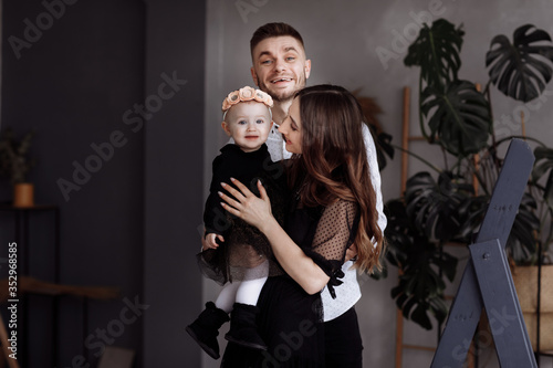 Portrait of beautiful young parents and their cute little daughter hugs, smiling indoors. mother's, father's, baby's day. concept of family. family look