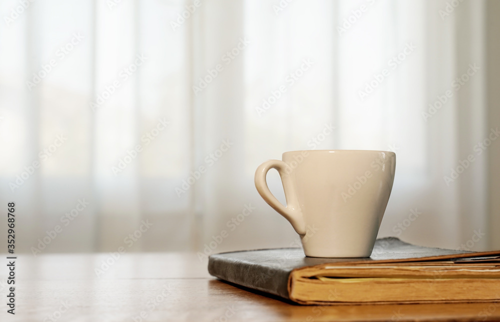 cup of coffee and book on a wooden table, window in the background cup of coffee and book on a wooden table, window in the background