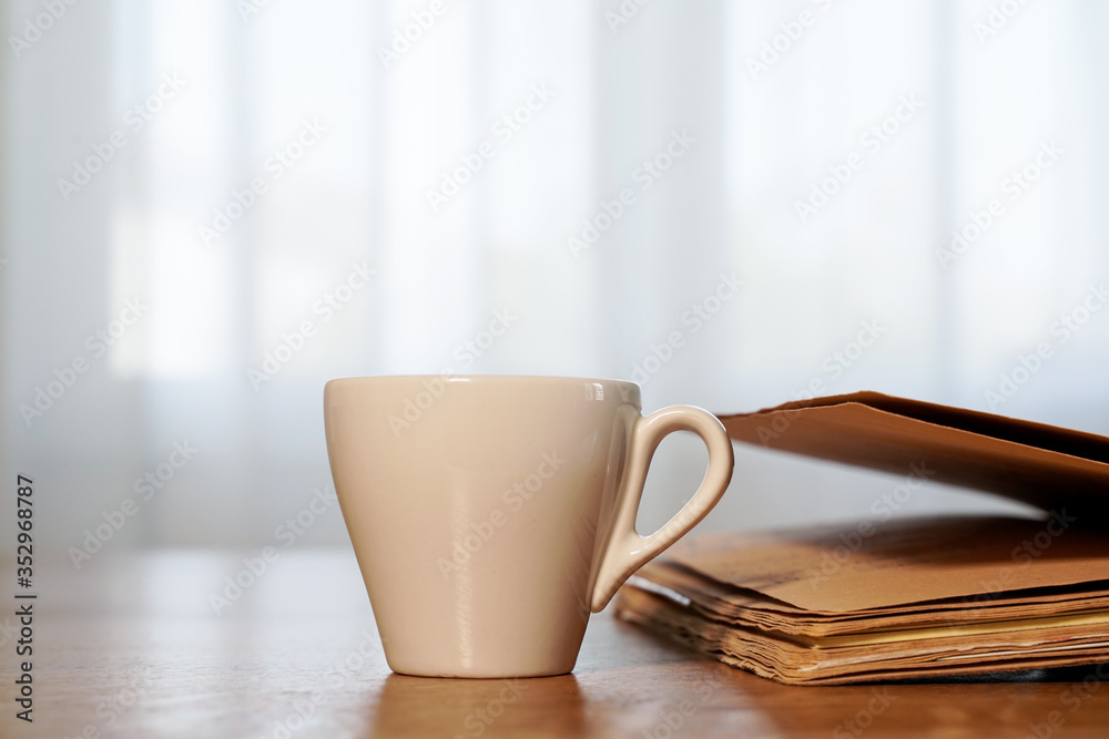 Fototapeta premium cup of coffee and book on a wooden table, window in the background