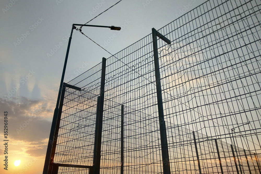 High wire mesh fence in restricted area on blue sky background. High wire mesh fence in restricted area on blue sky background.