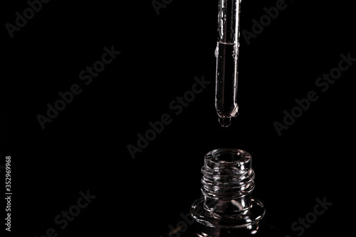 Close-up on a pipette with fluid and neck of a vial on black background
