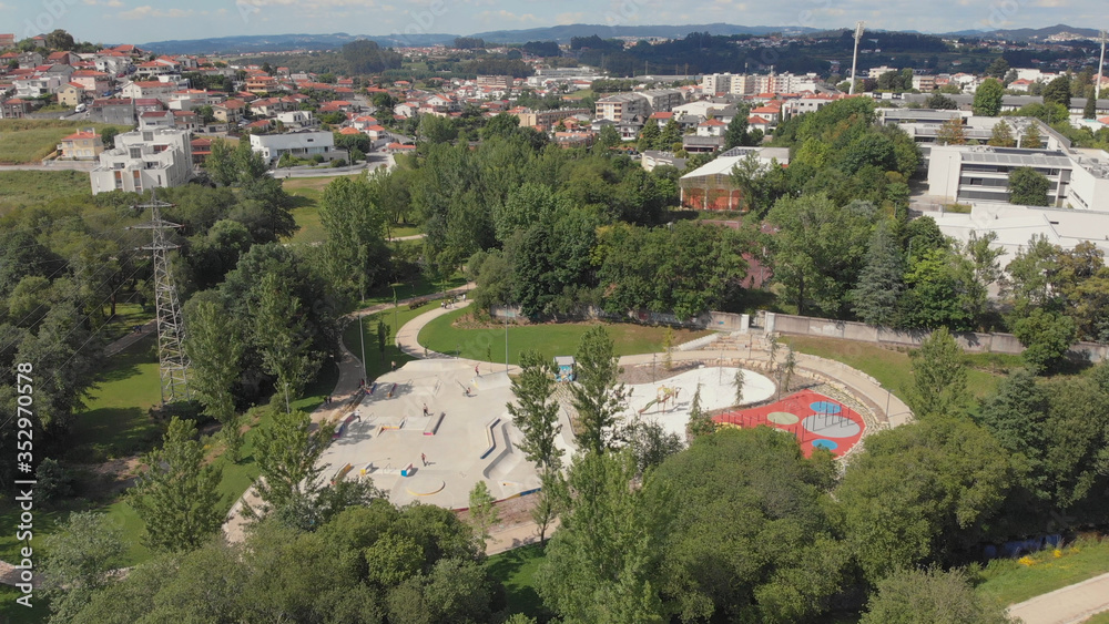 Amazing aerial view of the skate park in Santo Tirso city in Portugal with many skaters and bmx bikers on it. The Geao Urban Park with high school building in background.