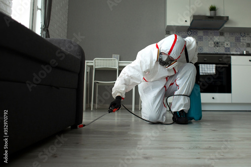 pest control. A worker in a protective suit cleans the room from cockroaches with a spray gun, the sanitary service disinfects the apartment with a chemical agent photo