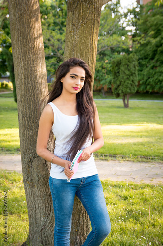 Young beautiful Indian girl stands in the park, holding a notebook in his hands. Portrait of a female student girl outdoors