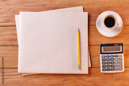 Top View of a Blank Newspaper on Wooden Desk or Table. Reading the News. Pen, Pencil, a Blank Notebook. Cup of coffe. Calculator. Copy space for text or Image.