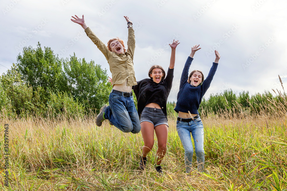 Summer holidays vacation happy people concept. Group of three friends boy and two girls jumping, dancing and having fun together outdoors. Picnic with friends on road trip in nature. Summer holidays vacation happy people concept. Group of three friends boy and two girls jumping, dancing and having fun together outdoors. Picnic with friends on road trip in nature.