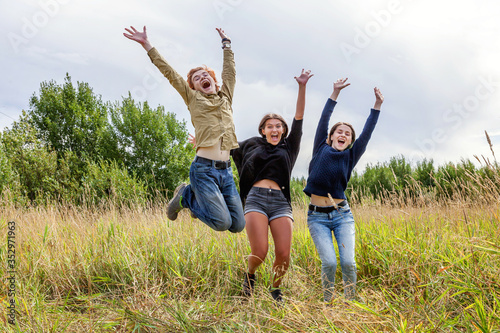 Summer holidays vacation happy people concept. Group of three friends boy and two girls jumping  dancing and having fun together outdoors. Picnic with friends on road trip in nature.