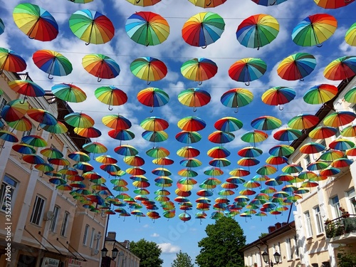 Multi-colored umbrellas in rows hang over the pedestrian street of the city on a May warm sunny day.