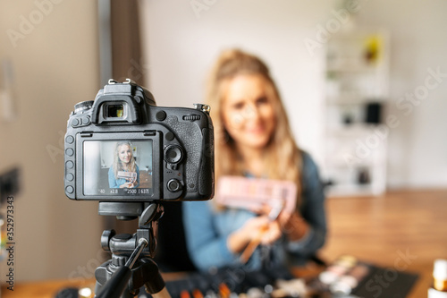 A young blonde woman talks about cosmetics and making a video for her beauty blog. Woman is holding a makeup palette and showing it at camera